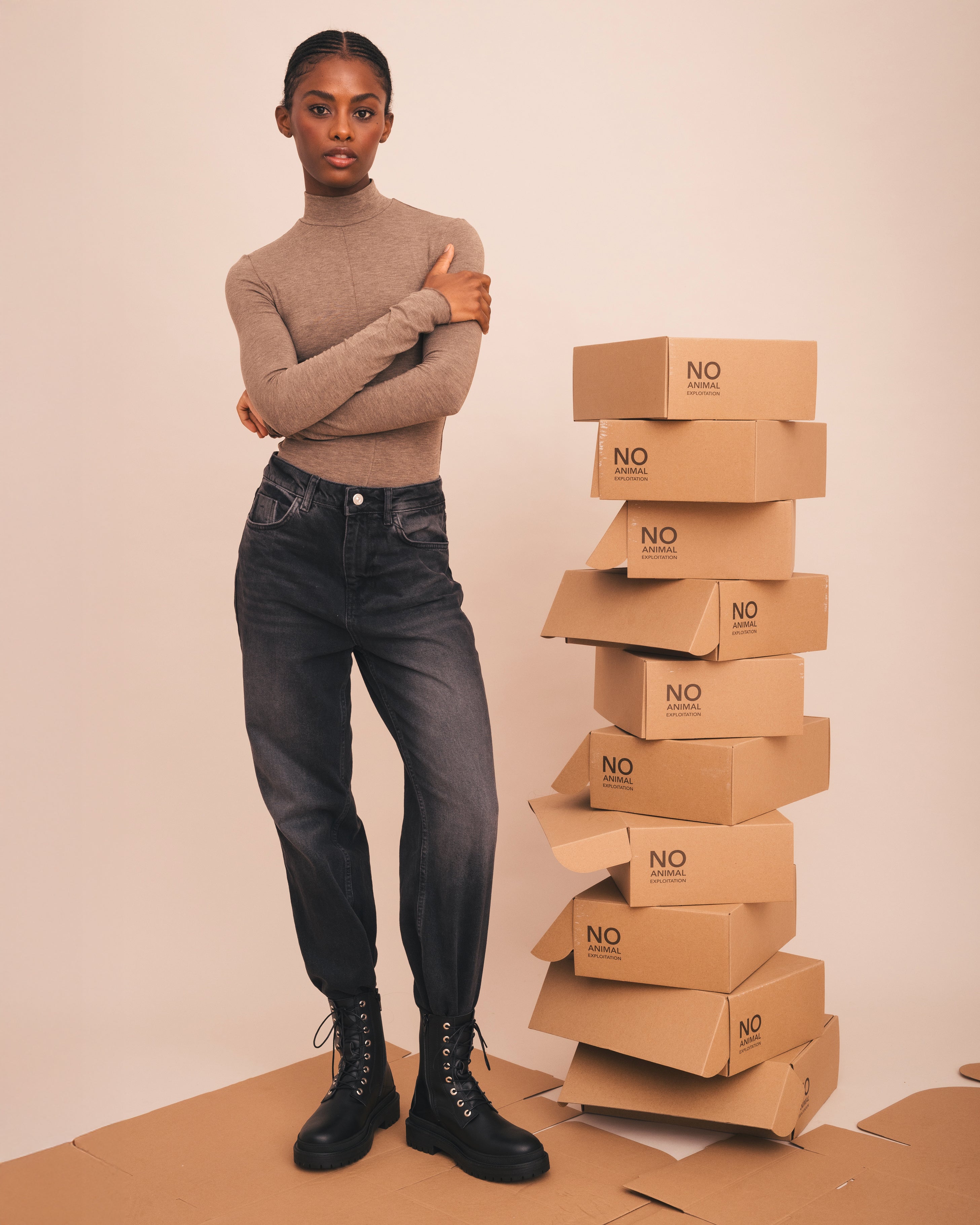 Woman standing next to a stack of cardboard boxes with 'NO' branding on a beige background