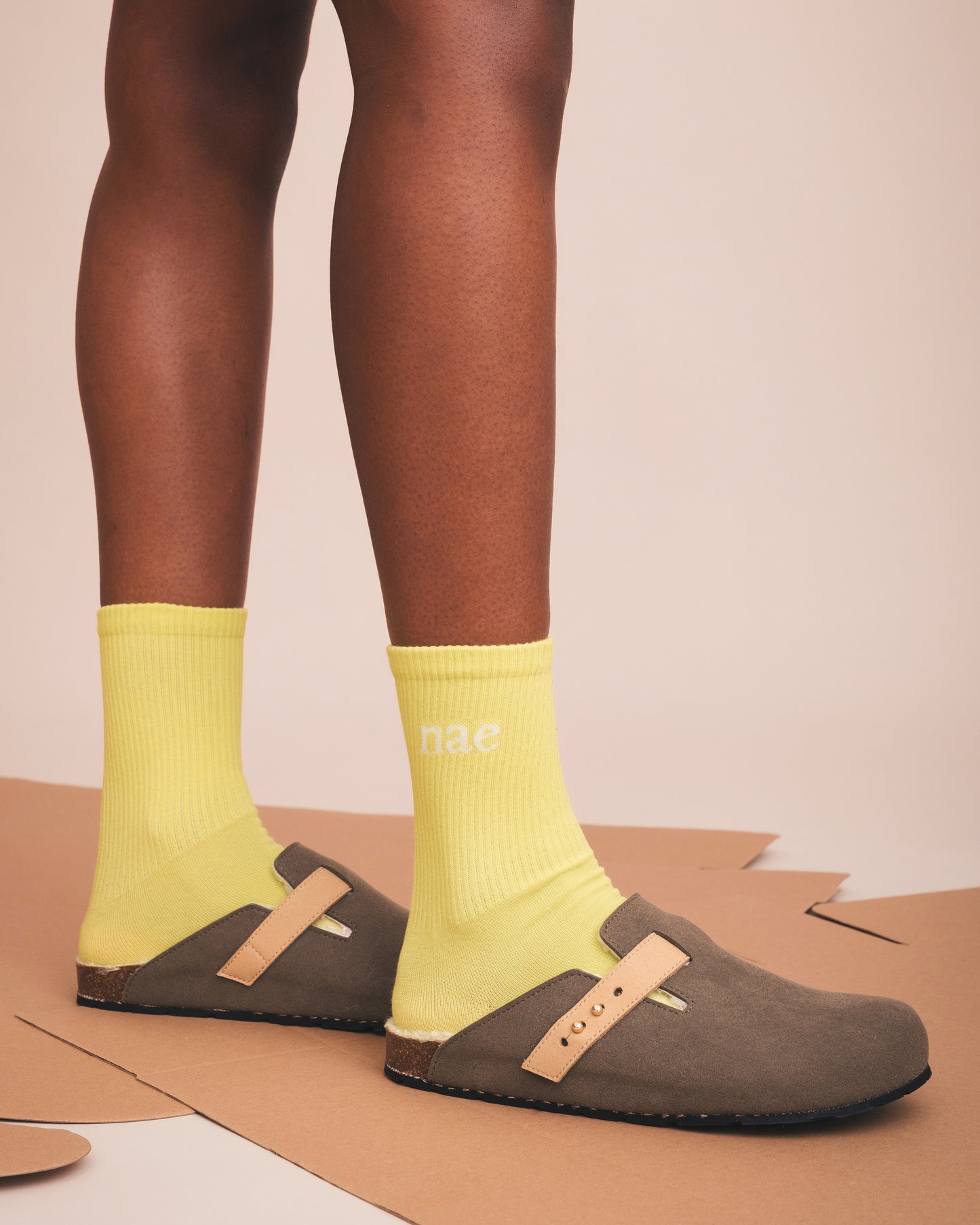 Person wearing yellow socks with 'nae' branding and brown clogs on a beige background