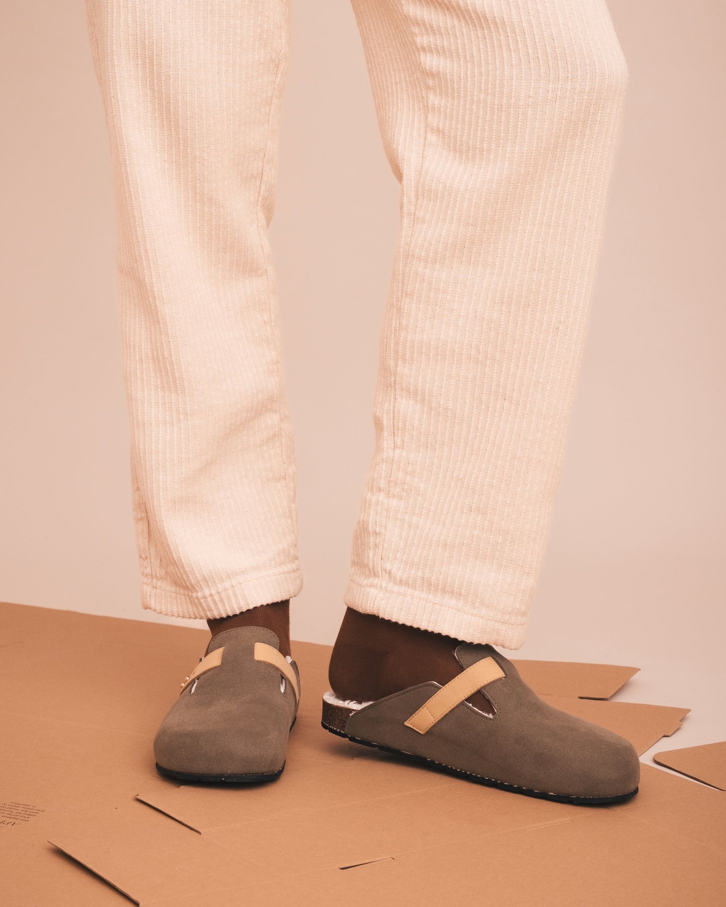 Brown slippers worn with white pants on a beige background