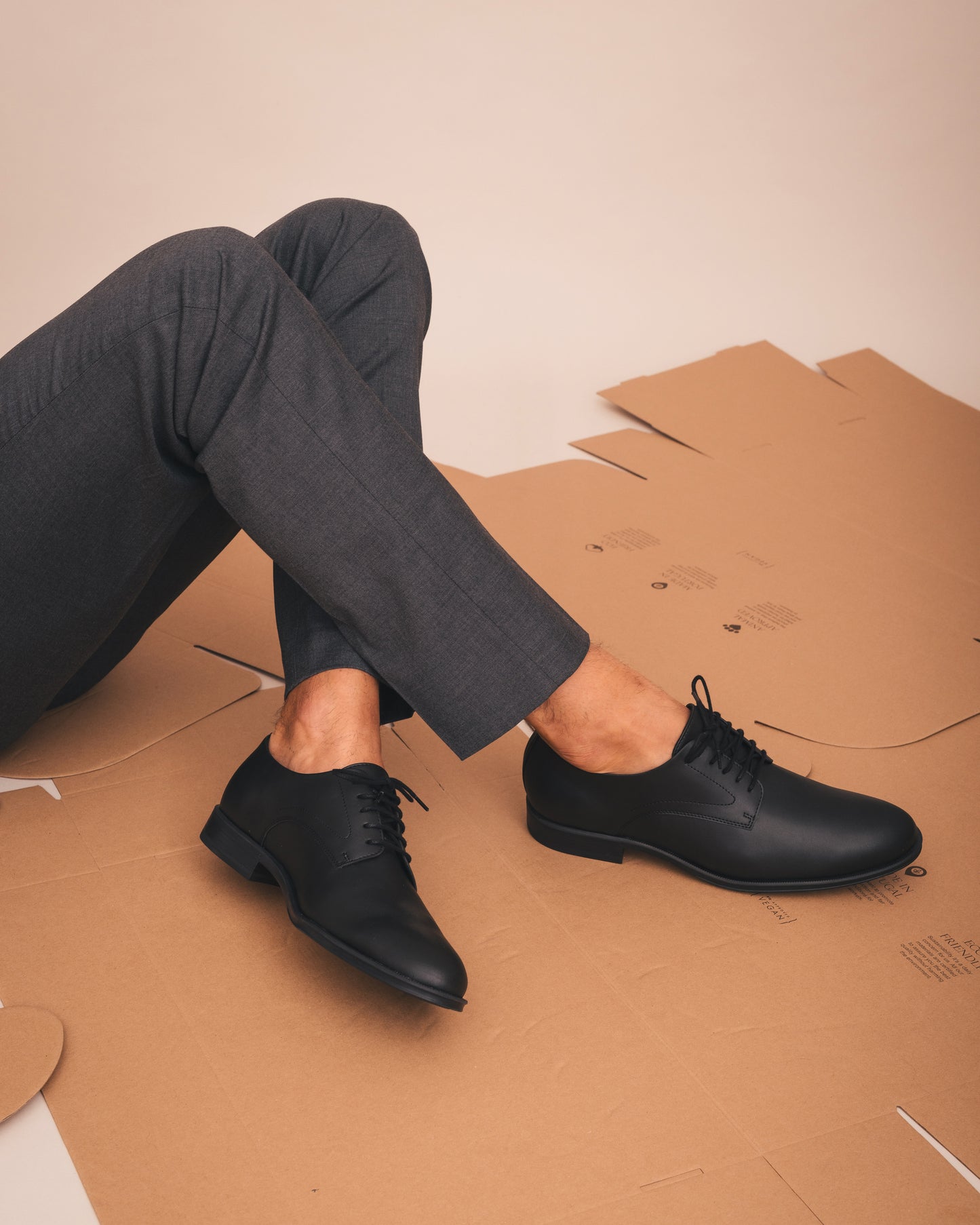 Person wearing black dress shoes sitting on cardboard with a plain background