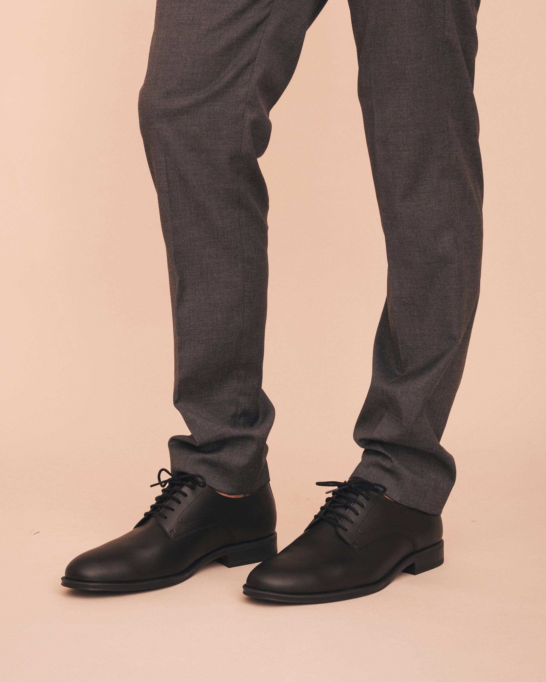 Black dress shoes worn with gray pants on a beige background