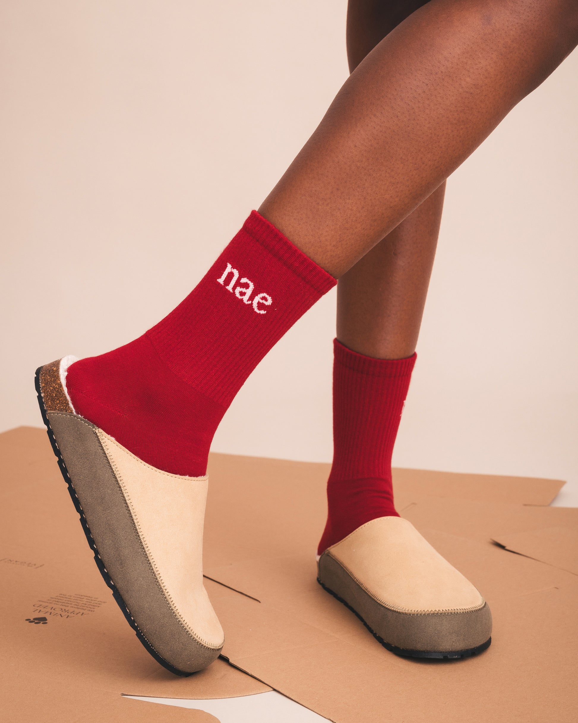 Red socks with 'nae' branding worn by a person on a cardboard surface.