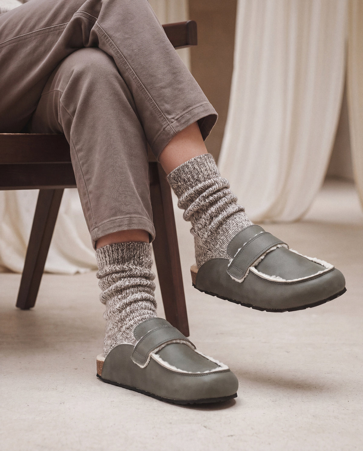 Person wearing gray loafers and patterned socks sitting on a chair.