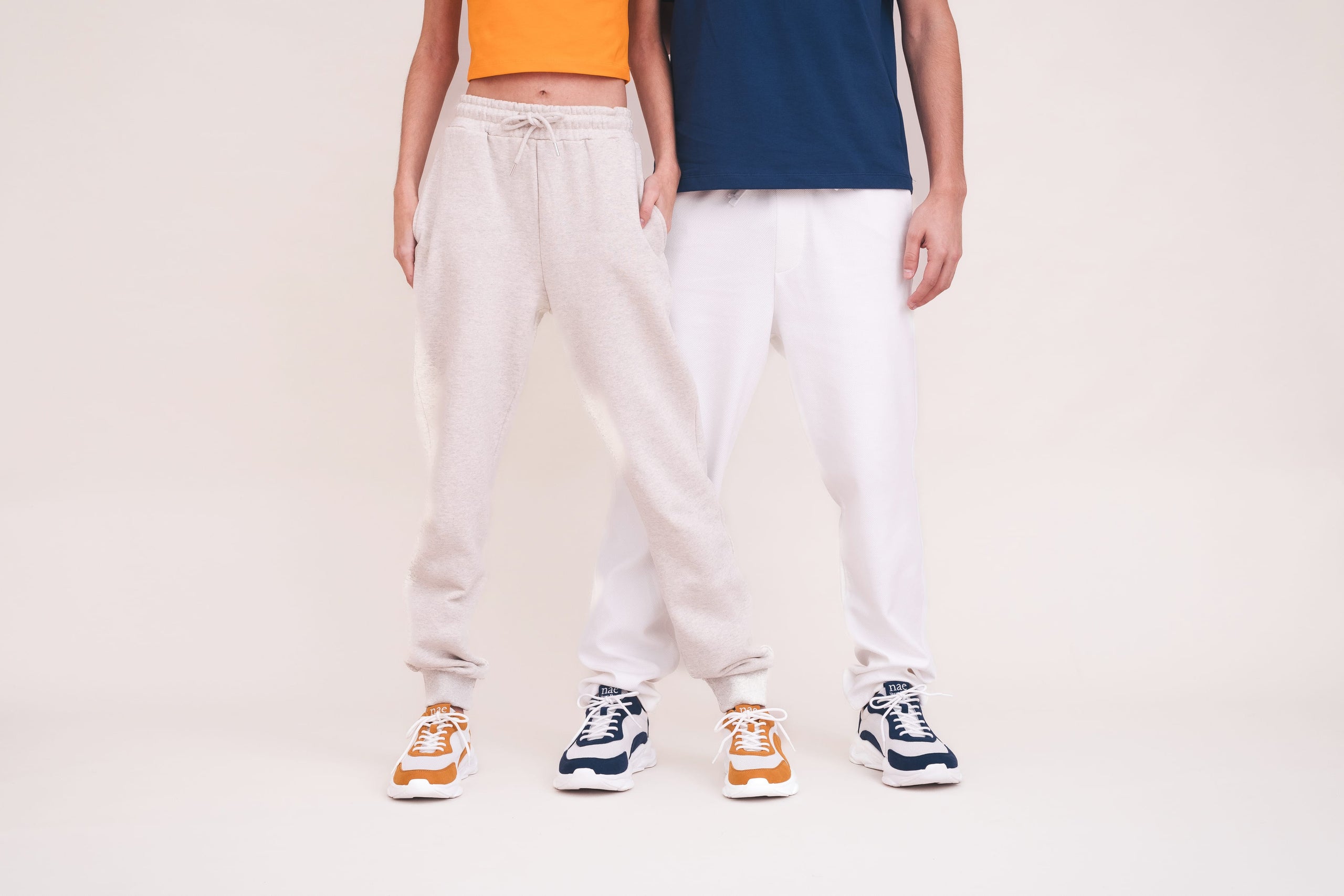 Two people wearing beige pants and colorful sneakers on a plain background